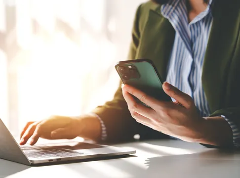 closeout of person working on laptop with phone in hand