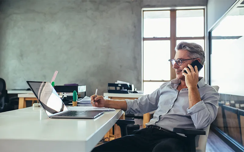 Middle-aged man sits at desk while talking on the phone