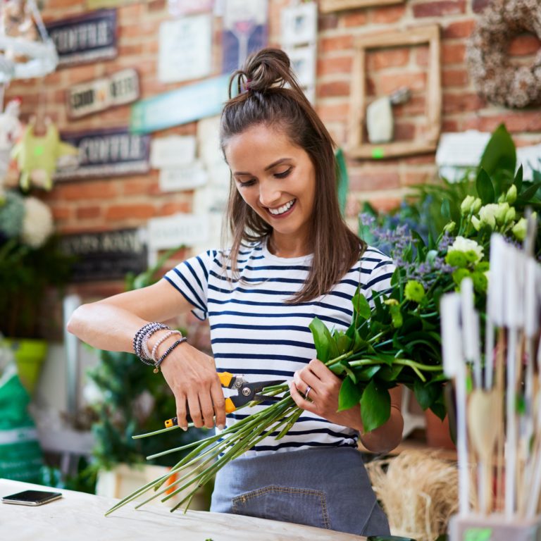 Cheerful young florist cutting flowers for bouquet at the counter