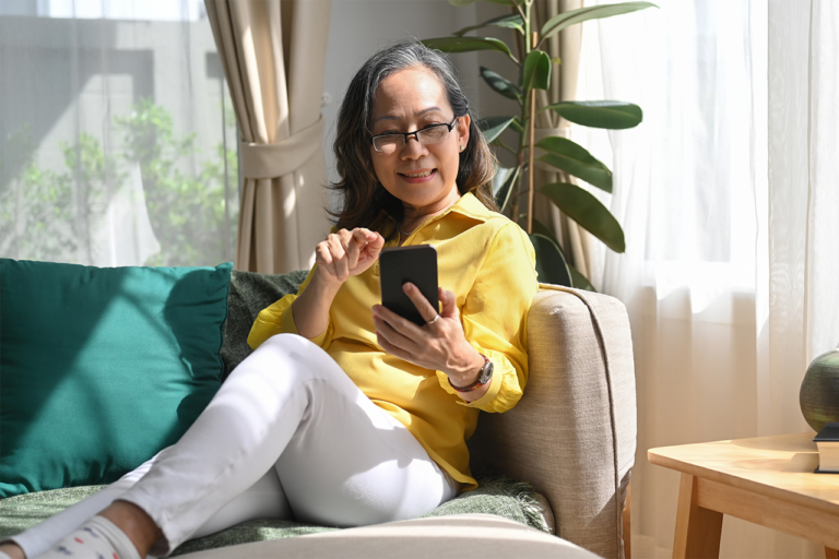 Older woman sitting on a couch using a smartphone.