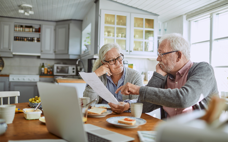 An elderly couple sitting at the kitchen table. They appear to be going over monthly bills and paying them.