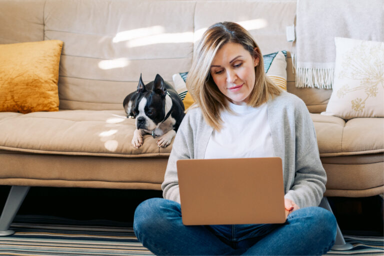 Young woman working from home with a boston terrier dog. Freelancer businesswoman using laptop at sunny room. Student learning and working at home.