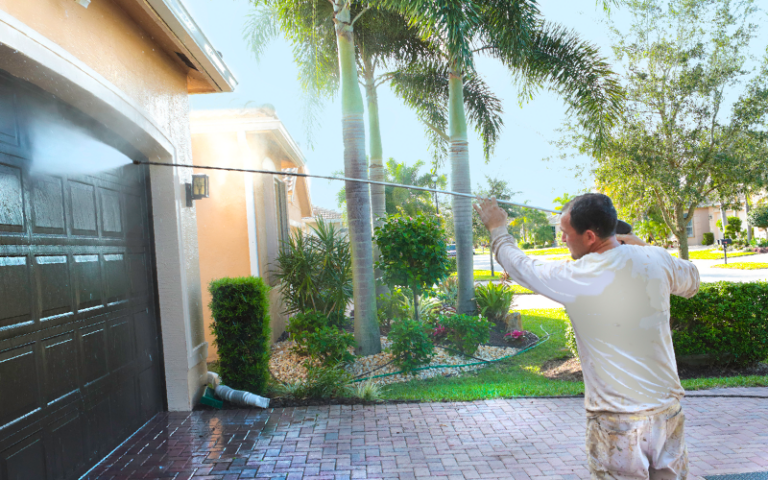 A man is seen power washing his garage door in the summer, which will drastically increase the home's curb appeal.