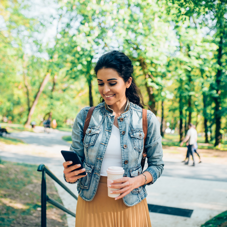 Young woman looking at phone while walking through a park.