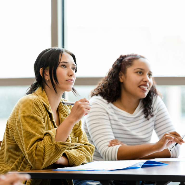 Two female students sitting in a classroom listening to a lecture.