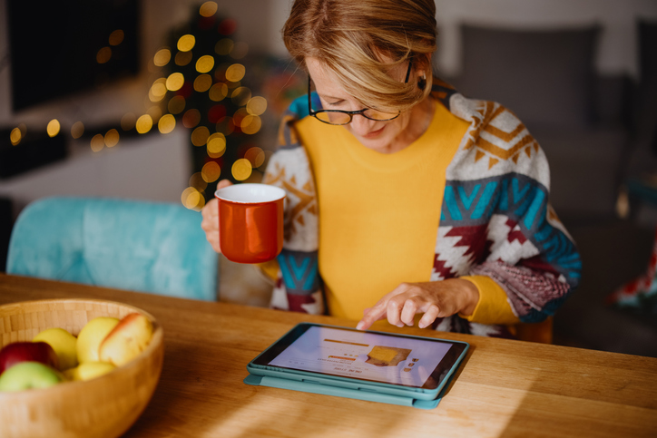 Woman enjoying online shopping and using digital tablet and credit card while sitting at dining table. Cybercriminals.