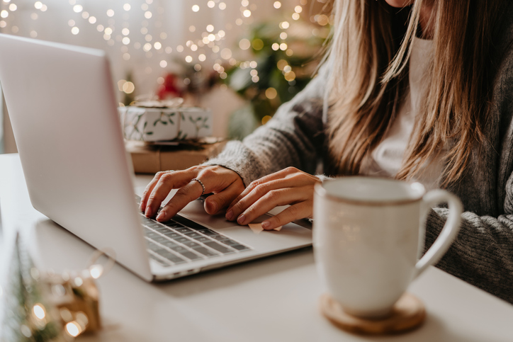 Close up of woman hands with, gifts, coffee cup and laptop. Online shopping at Christmas holidays. Freelance girl working from home office. Female typing at laptop computer. Christmas moments.