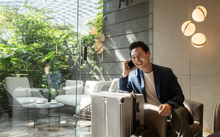 Smiling man using a smartphone in an airport lounge with luggage, symbolizing secure travel and digital connectivity.