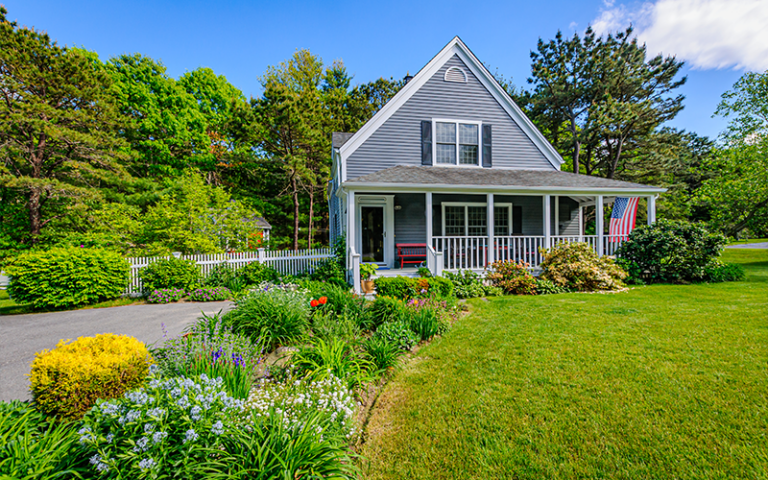 Charming single-family home with front porch, spring landscaping, and American flag—ideal representation of spring homeownership in a suburban neighborhood.