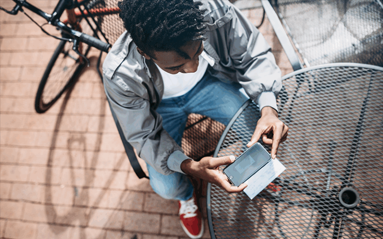 Man using mobile deposit feature to deposit check outside at a cafe table.